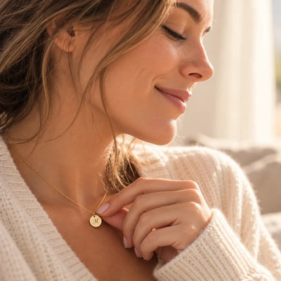 Mujer sonriendo con los ojos cerrados mientras acaricia su collar con una medalla dorada personalizada